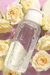 Wet bottle of micellar water and beautiful white roses on pink background, top view