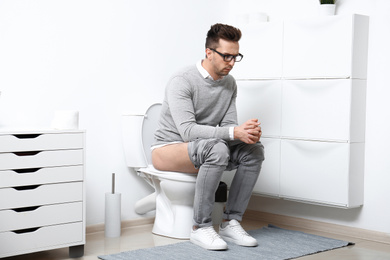 Upset man sitting on toilet bowl in bathroom