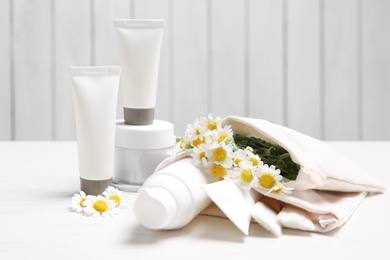 Set of different cosmetic products and chamomile flowers on white table