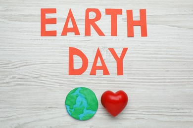 Words Earth Day, plasticine planet and decorative heart on white wooden table, flat lay