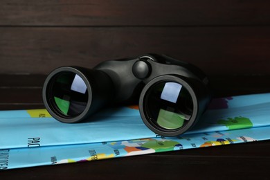 Modern binoculars and map on wooden table, closeup