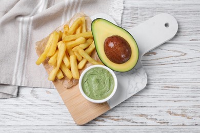 Serving board with french fries, guacamole dip and avocado on white wooden table, top view