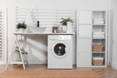 Laundry room interior with modern washing machine and shelving unit near white wall