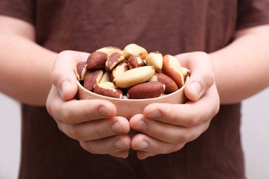 Photo of Woman holding bowl with tasty Brazil nuts on blurred background, closeup
