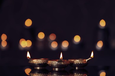 Photo of Lit diyas on table against blurred lights. Diwali lamps
