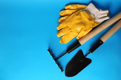 Gardening gloves, trowel and rake on light blue background, flat lay. Space for text