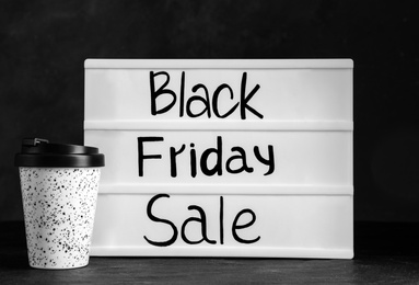 Reusable coffee cup and lightbox with words Black Friday Sale on table against dark background