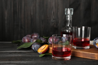 Photo of Delicious plum liquor and ripe fruits on black wooden table. Homemade strong alcoholic beverage