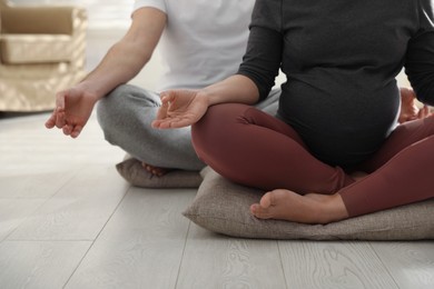Young pregnant woman with her husband practicing yoga at home, closeup