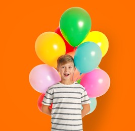 Happy little boy holding bunch of colorful balloons on orange background