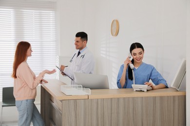 Receptionist talking on phone while doctor working with patient in hospital