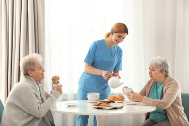 Nurse assisting while elderly women having breakfast at retirement home