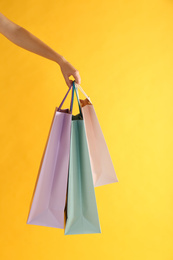 Woman with paper shopping bags on yellow background, closeup
