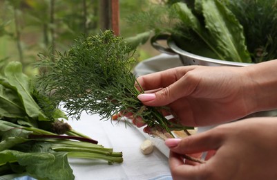 Woman with fresh green herbs and twine indoors, closeup