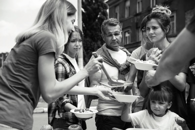 Volunteers serving food for poor people outdoors, black and white effect