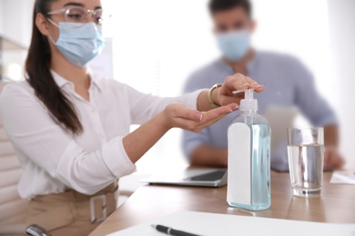 Office worker in protective mask using sanitizer at table, focus on hands. Personal hygiene during COVID-19 pandemic