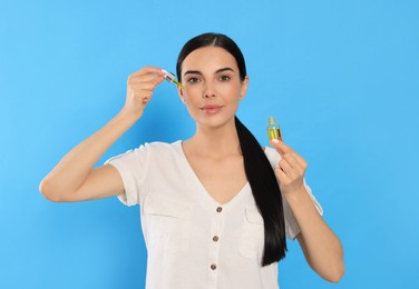 Young woman applying essential oil onto face on light blue background