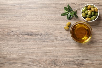 Glass bowl of oil, ripe olives and green leaves on wooden table, flat lay. Space for text