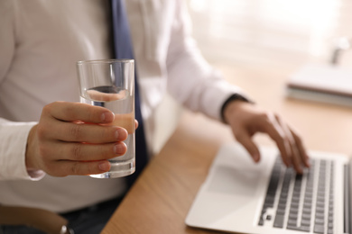 Office employee with glass of water at workplace, closeup