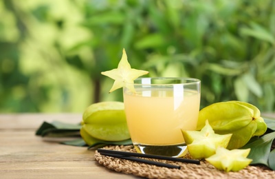 Delicious carambola juice and fresh fruits on wooden table against blurred background. Space for text