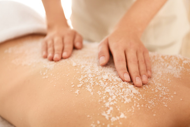 Young woman having body scrubbing procedure with sea salt in spa salon, closeup