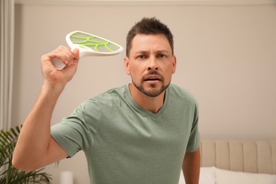 Man with electric fly swatter in bedroom. Insect killer