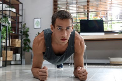 Handsome man doing plank exercise on floor at home