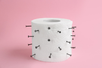 Roll of toilet paper with nails on pink. Hemorrhoid problems