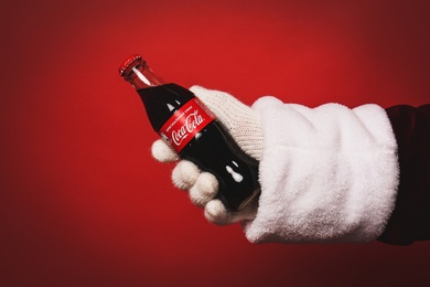 MYKOLAIV, UKRAINE - JANUARY 18, 2021: Santa Claus holding Coca-Cola bottle in hand on red background, closeup