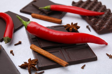 Photo of Delicious chocolate, fresh red chili peppers and spices on white table, closeup
