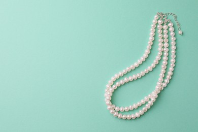 Photo of Elegant pearl necklace on turquoise background, top view. Space for text