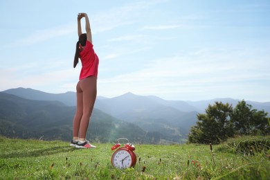 Woman doing morning exercise in mountains, focus on alarm clock