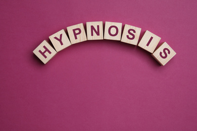 Wooden blocks with word HYPNOSIS on magenta background, flat lay