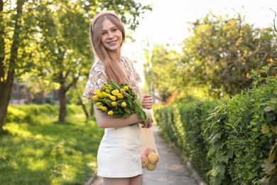 Beautiful teenage girl with bouquet of yellow tulips and apples in park on sunny day