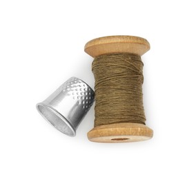 Photo of Thimble and spool of brown sewing thread isolated on white, top view