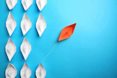 Photo of Orange paper boat floating away from others on light blue background, flat lay with space for text. Uniqueness concept