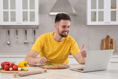 Photo of Smiling man making pizza while watching cooking online course in kitchen. Time for hobby