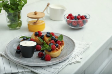 Delicious cottage cheese pancakes with fresh berries, mint and sour cream on white table. Space for text