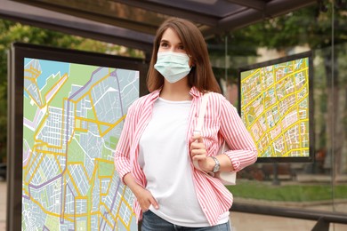 Young woman in protective mask waiting for public transport at bus stop