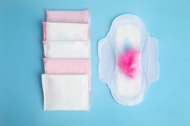 Menstrual pads and pink feather on light blue background, flat lay
