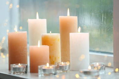 Beautiful burning candles and fairy lights at windowsill on rainy day