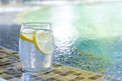 Refreshing water with lemon on edge of swimming pool, space for text