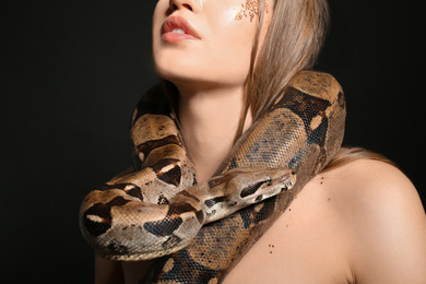 Photo of Beautiful woman with boa constrictor on black background, closeup
