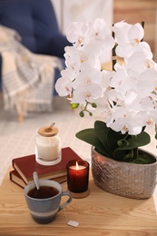 Beautiful white orchids, books, cup of tea and candles on table in room. Interior design
