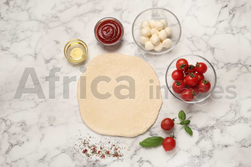 Photo of Raw pizza dough and other ingredients on white marble table, flat lay