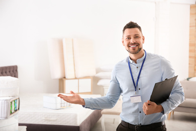 Photo of Happy salesman with clipboard in mattress store. Space for text