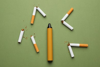 Disposable electronic smoking device surrounded by broken cigarettes on olive background, flat lay