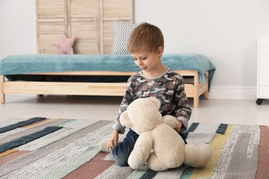 Cute little boy playing with teddy bear at home