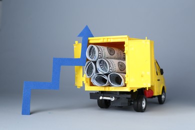 Economic profit. Arrow and toy truck with banknotes on light grey background