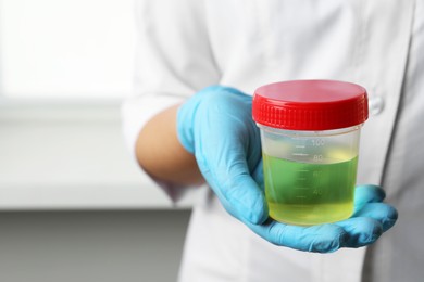 Doctor holding container with urine sample for analysis indoors, closeup